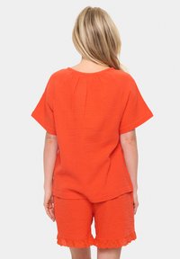 Dvojdielny outfit v žiarivej oranžovej, pozostávajúci z textúrovanej blúzky s krátkymi rukávmi a zodpovedajúcich šortiek s čipkovým lemom.