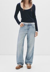 Top de manga larga azul marino con ribete blanco, combinado con jeans de mezclilla de pierna ancha en azul claro. Zapatos marrones de cordones completan el atuendo.