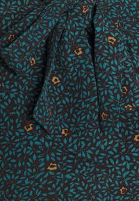 Svart tyg med ett tätt mönster av teal-löv och små gyllene blommor som accent. Har en framträdande rosettdetalj. Mjukt, texturerat material.