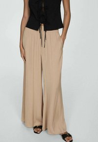 Pantalon beige à jambes larges en tissu léger, doté d'une taille élastique et de poches latérales. Associé à un haut noir à lacets.