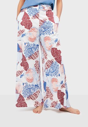 Pantalones de pierna ancha con patrones de vida marina y corales en rojo, azul y naranja, utilizados descalzo por una persona con las manos en los bolsillos.