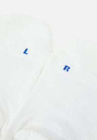 Calze bianche in tessuto texturizzato, con le lettere blu "L" e "R" per sinistra e destra. Il design prevede aree rinforzate nella punta e nel tallone.