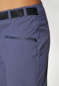 Ljubičaste trenirke od prozračnog materijala s modernim dizajnom, koje imaju zipper džep na boku i crnu elastiku.