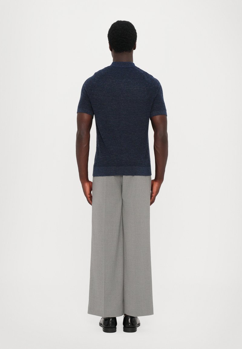 Navy short-sleeve knit polo shirt paired with light gray wide-leg trousers and black shoes, viewed from the back against a white background.