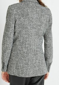 Blazer nero e bianco testurizzato con una vestibilità sagomata, colletto a punta e polsini con bottoni, caratterizzato da un sottile motivo tessuto.