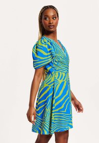 Short-sleeve dress in bright blue with bold green abstract stripes, featuring a V-neckline and a flared skirt for a relaxed fit.