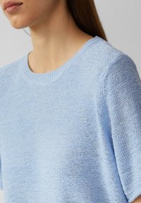 Lichtblauwe gebreide trui met een ronde hals, korte mouwen en een textuurpatroon, die een zachte stof en een relaxte pasvorm laat zien.