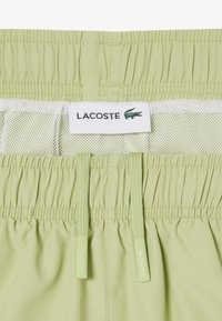 Shorts de bain Lacoste vert clair avec taille élastique, doublure en filet blanc et cordons de serrage brandés.