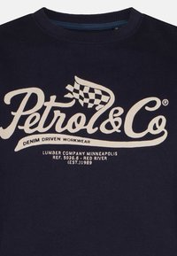 Felpa girocollo blu navy con logo "Petrol & Co", grafica a bandiera a scacchi e testo che fa riferimento all'abbigliamento da lavoro in denim e a una compagnia forestale di Minneapolis.