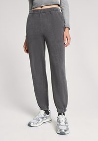 Szare spodnie dresowe wykonane z miękkiego materiału, z elastycznym pasekiem w talii, zwężanymi kostkami i luźnym krojem. Noszone z srebrnymi butami sportowymi.
