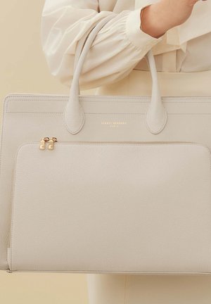 Sac tote en cuir gris avec poignées supérieures, doté d'une poche zippée sur le devant ornée de quincaillerie dorée et du logo de la marque. Fini lisse et texturé.