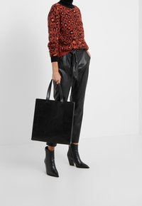 Zwarte leren totebag met twee handvatten, eenvoudige rechthoekige vorm, gladde textuur. Draag met een leopardprint trui en strakke zwarte broek.