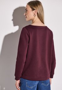 Felpa bordeaux con scollatura rotonda, maniche lunghe e polsini a costine. Abbinata a jeans azzurri chiari, con una classica texture denim.