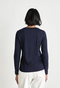 Langermet t-skjorte i marineblått laget av myk bomull, med rund hals og tettsittende design, vist fra baksiden.