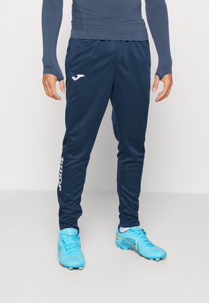 Navy athletic pants made of smooth fabric, featuring a white logo on the thigh and fitted design. Worn with bright blue soccer cleats.