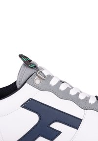 White sneaker with navy blue accents and gray suede details. Features a textured gray pull tab and white laces. Subtle stitching detail.