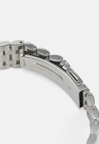 Montre en acier inoxydable avec finition polie, dotée d'un bracelet à maillons ovales, d'une fermeture à clapet et d'un détail gravé à l'intérieur.