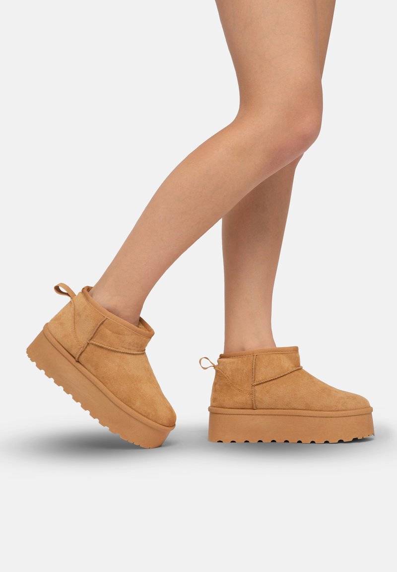 Botines de ante en tono beige con suela de plataforma sólida y estriada, y tirador en la parte trasera. Presentan un diseño simple y redondeado con un detalle minimalista.