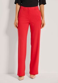 Rote, hochtaillierte, weitgeschnittene Hosen aus einem glatten, dehnbaren Stoff. Verfügt über Seitentaschen und einen maßgeschneiderten Bund. Getragen mit hautfarbenen Absätzen.