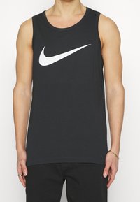 Svart ärmlös linne i bomull, med en vit Nike swoosh-logga på framsidan. Slät textur, rund halsringning och rak fåll.
