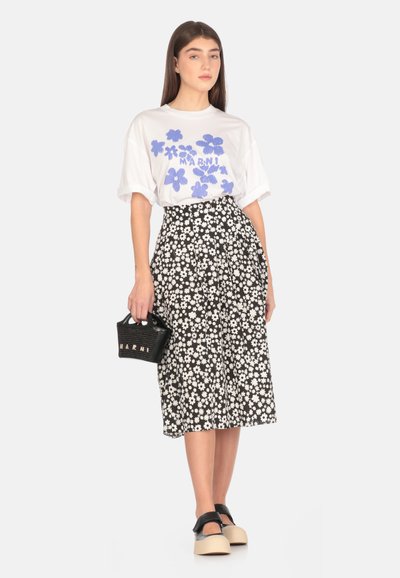 T-shirt bianca con stampa floreale blu, gonna floreale nera, borsa nera e scarpe con plateau beige. La gonna presenta margherite bianche su uno sfondo nero.