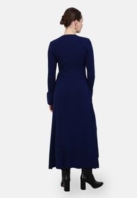 Abito maxi a righe navy con maniche lunghe, corpino aderente e gonna svasata, abbinato a stivaletti neri con tacco.