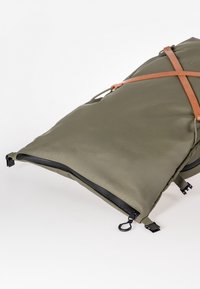 Grand sac étanche vert olive à rabat roulant avec des brides croisées marron, des fermetures éclair noires et des boucles en plastique sur fond blanc.