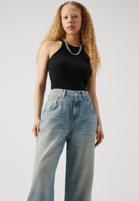 Black ribbed tank top paired with light blue, high-waisted, wide-leg jeans. Notable silver chain necklace and relaxed fit overall.