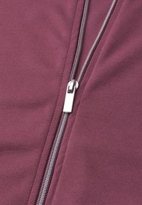 Close-up of a silver zipper partially zipped on a maroon fabric garment, showing knit texture and stitching detail.