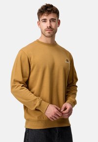 Sennepsfarvet crewneck sweatshirt lavet af blødt stof, med ribbede manchetter og kant, samt et lille logo på venstre bryst.