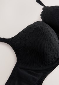 Reggiseno nero con dettagli in pizzo e coppe in tulle strutturato. Design con ferretto, spalline regolabili e fascia in tessuto liscia.