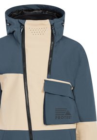 Blaue und beige wasserdichte Jacke mit hohem Kragen, durchgehendem Reißverschluss und einer großen Klappentasche. Verfügt über Belüftungslöcher und Branding auf der Tasche.