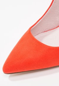 Escarpin à bout pointu en daim rouge avec une doublure intérieure lisse et un extérieur texturé. Silhouette élégante avec une coupe basse et un design minimaliste.
