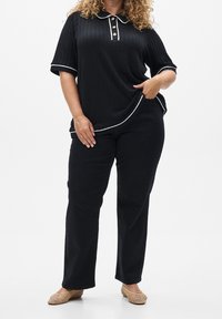 Czarna teksturowana koszulka polo z białym kołnierzykiem i trzema złotymi guzikami, w zestawie z czarnymi spodniami i beżowymi plecionymi balerinami.