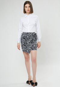 Witte blouse gecombineerd met een aansluitende zwart-wit gestreepte rok, accenten met een strik aan de zijkant, en zwarte sandalen met een strik.