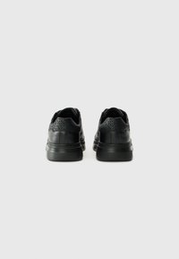 Black sneakers with textured back panel, smooth leather upper, and rubber sole. Designed with subtle branding and contrasting stitching.