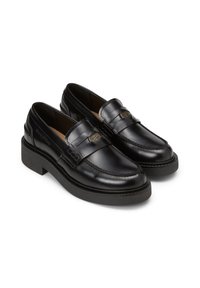 Mocassins en cuir noir avec un bout rond et une semelle en caoutchouc noir contrastante. Présentent une sangle décorative et un logo subtil sur le côté.