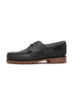 Zapato náutico de cuero negro con detalles de cordones, puntera redonda, suela de goma marrón texturizada y lados de cuero cosidos.
