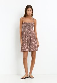 Blumenkleid in gedämpftem Lila, mit verstellbaren Trägern, gerafftem Oberteil und weit schwingendem Rock. Leichter Stoff mit weicher Textur.
