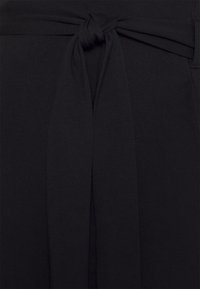 Cinto de tecido preto com detalhe de nó. Textura suave com forma afunilada, projetado para prender e ajustar na cintura.