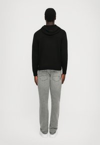 Sort hættetrøje med tekstureret strikket mønster, parret med grå denim jeans med markerede baglommer og afslappet pasform.