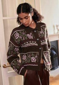 Bruine cardigan met een patroon en bloemontwerpen in roze en groen, met een kraag, knoopsluiting en geribde manchetten. Getextureerde brei-stof.