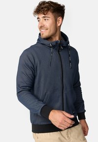 Marineblauer Zip-Hoodie mit vorderen Taschen, Kapuze mit Kordelzug und schwarzen Rippbündchen. Besitzt einen strukturierten Stoff mit subtilen Musterdetails.