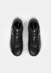 Baskets de sport noires avec une tige en maille respirante, dotées d'un système de laçage de soutien, d'une semelle intermédiaire rembourrée et d'une semelle extérieure en caoutchouc blanc.