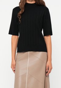 Haut noir en maille côtelée avec manches courtes et col montant, associé à une jupe beige texturée avec panneaux géométriques.