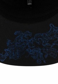 Casquette noire avec un motif de ligne abstraite bleue, tissu texturé, visière courbée et réglable. Étiquette visible à l'intérieur.