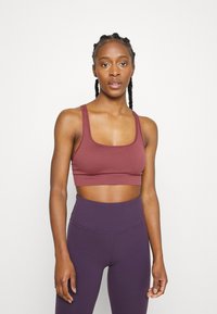 Top desportivo cor bordeaux com decote quadrado, textura canelada e alças largas, combinado com leggings roxas de cintura alta que apresentam detalhes de costura.