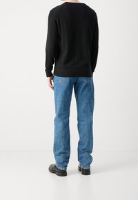 Musta pitkähihaisen neulepuseron pyöreä kaula-aukko, yhdistetty vaaleansinisiin farkkuihin, rento istuvuus, suora lahje, ja mustat nilkkurit.