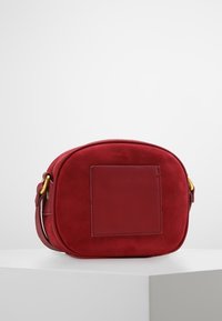 Rød suede crossbody taske med en rund form, glat tekstur og et læderdetalje-panel foran. Inkluderer guldfarvet hardware.