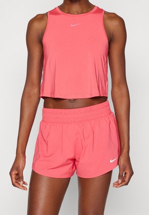 Frau trägt ein korallenrosa ärmelloses, kurzes Sporttop und passende Shorts mit elastischem Bund und weißen Nike-Logos.